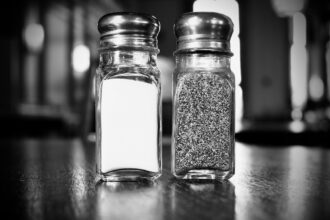Elderly person adding salt to meal at dining table, representing study findings on salt consumption habits