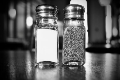 Elderly person adding salt to meal at dining table, representing study findings on salt consumption habits