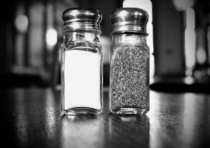 Elderly person adding salt to meal at dining table, representing study findings on salt consumption habits